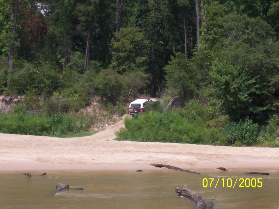 White and red SUV parked on a dirt path near trees, viewed from the rear