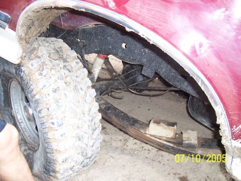1987 Ford Bronco - Mud-covered tire and suspension components are visible in the wheel well of a red SUV.