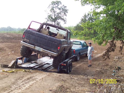 1987 Ford Bronco - A dark blue pickup truck is being loaded onto a trailer, with another pickup truck and a man observing the scene.
