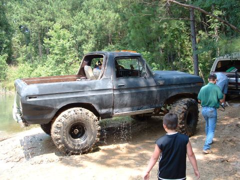 1993 Ford Bronco - Modified Ford Bronco with large tires is partially submerged in water and mud.