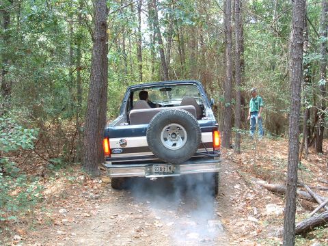 1993 Ford Bronco - A Ford Bronco navigates a wooded trail, its rear tires kicking up dust as it drives away.