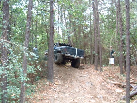 1993 Ford Bronco - A dark colored truck navigates a wooded trail with two onlookers.