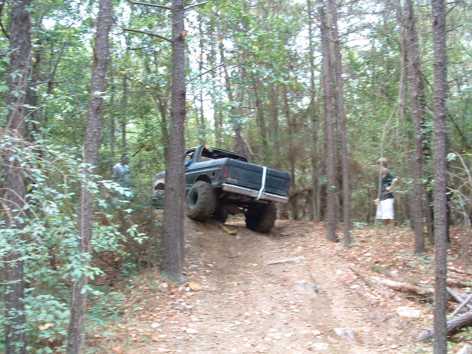 Truck going up a dirt path in woods. Two people are visible