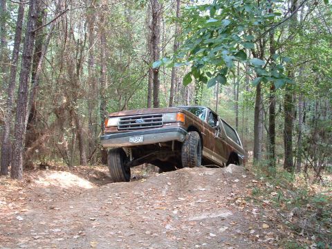 1993 Ford Bronco - A brown Ford Bronco navigates an off-road trail in a wooded area.