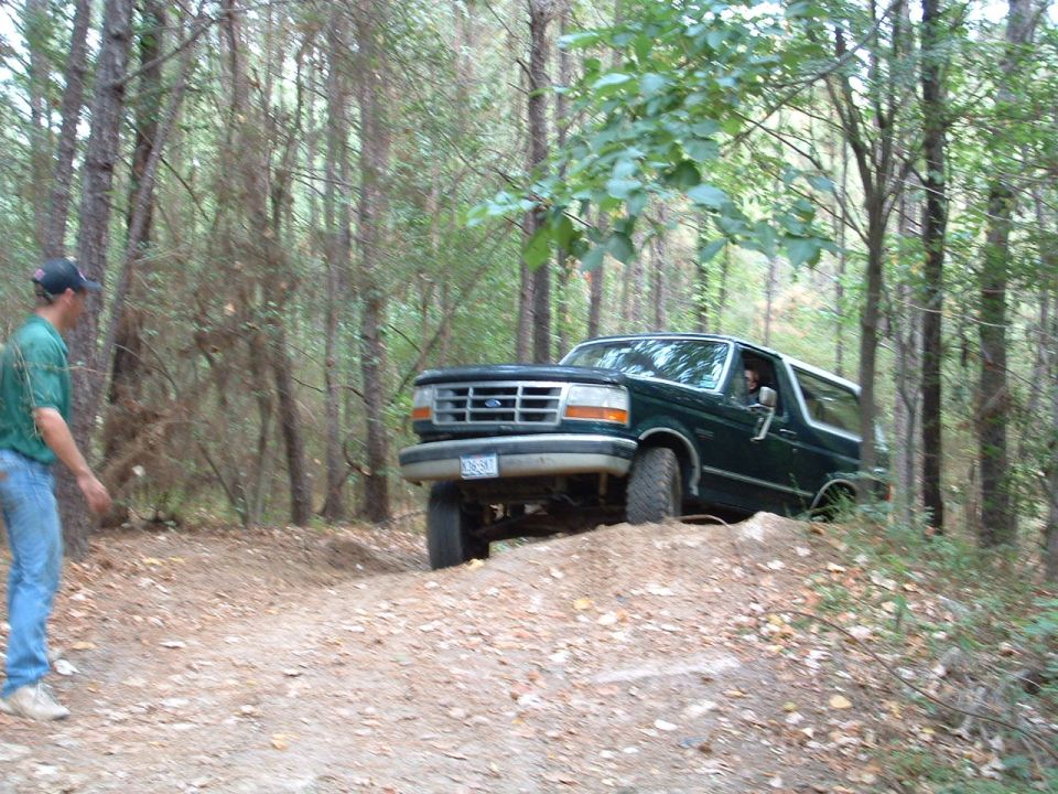 Dark green 1993 Ford Bronco driving on a dirt trail through trees