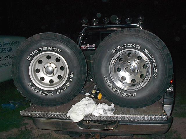 Two Maxxis Buckshot Mudder tires on chrome rims are loaded in the bed of a pickup truck