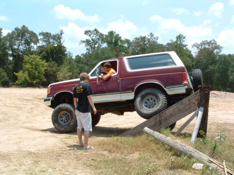 1993 Ford Bronco - A maroon and white Ford Bronco navigates an off-road obstacle, with two people observing the action.