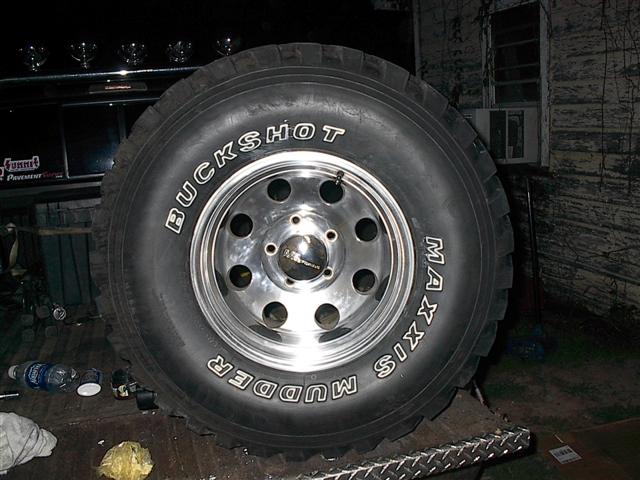 Maxxis Buckshot Mudder tire on a chrome rim, with part of a dark vehicle visible behind it