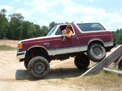 1993 Ford Bronco - A man drives a lifted 1993 Ford Bronco up a wooden ramp during an off-road excursion.