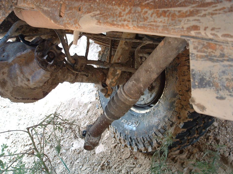 Undercarriage view of a muddy off-road vehicle, showing the rear axle, driveshaft, and tire