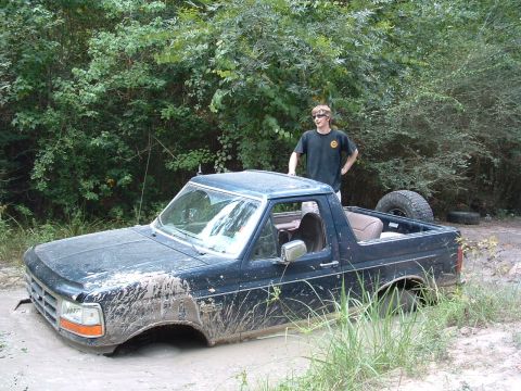 1993 Ford Bronco - A 1993 Ford Bronco is stuck deep in mud, with a person standing beside it observing the situation.