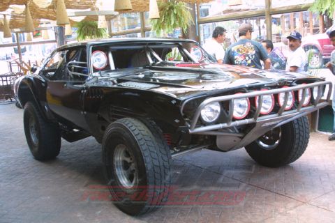 1990 Ford Bronco - Black muscle-car-style off-road race vehicle with a tube bumper, multiple driving lights and off-road tires at an outdoor venue.