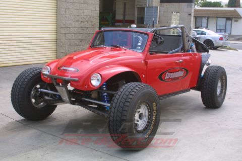 1990 Ford Bronco - red VW Beetle-bodied off-road buggy with long-travel front suspension and BFGoodrich tires sits in a garage.