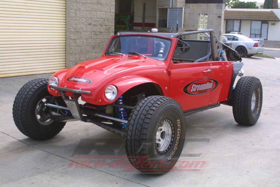 Red Volkswagen Beetle-bodied off-road buggy with exposed long-travel suspension in a shop