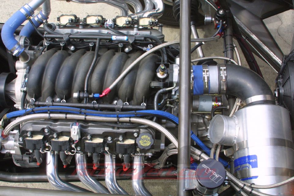 Close-up of a V8 engine bay with blue silicone hoses, braided lines and chrome intake