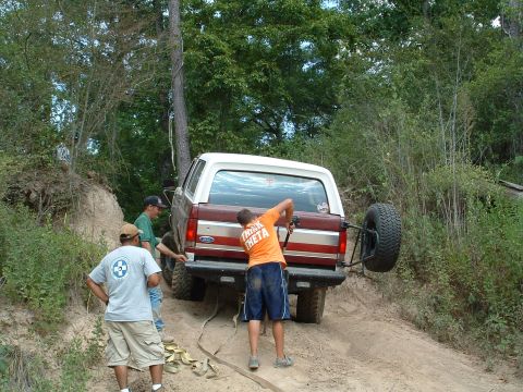 1993 Ford Bronco - Three people assist a maroon and white Ford Bronco that is stuck on a steep dirt incline.