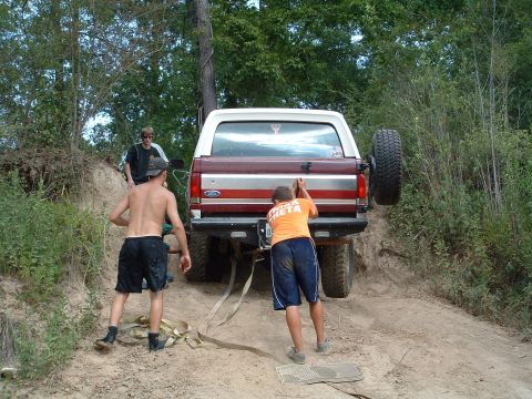 1993 Ford Bronco - A group of people are working together to free a Ford Bronco stuck on a muddy hill.