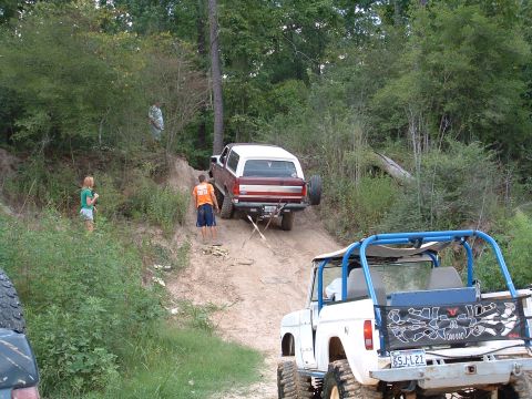 1993 Ford Bronco - Two off-road vehicles navigate a steep, sandy incline surrounded by dense foliage.