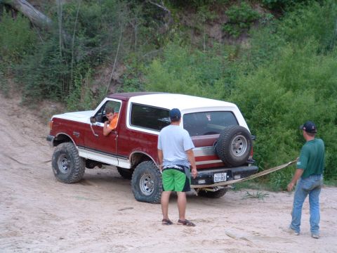 1993 Ford Bronco - A red and white SUV with off-road tires is being towed on a dirt path.