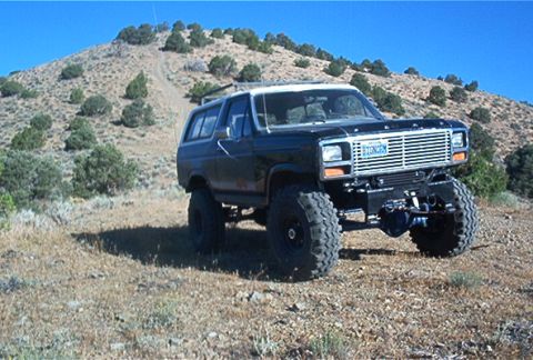 1986 Ford Bronco - This modified Ford Bronco sits on a dry, scrub-covered hillside under a clear blue sky.