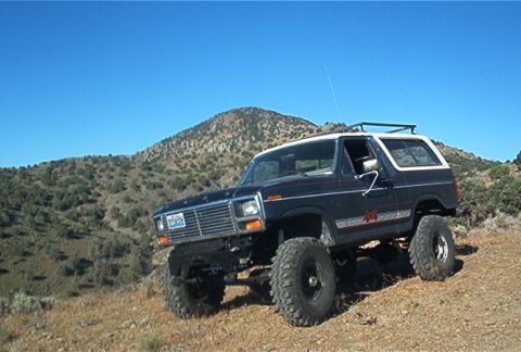 1986 Ford Bronco - This lifted 1980 Ford Bronco is ready for off-road adventures, parked on a dusty hillside under a clear blue sky.