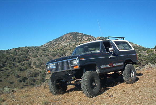 Dark blue 1980 Ford Bronco with lifted suspension and off-road tires parked on a dirt slope