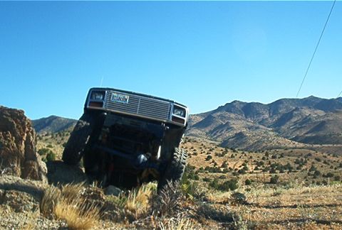 1986 Ford Bronco - An off-road vehicle navigates a steep, rocky incline under a clear blue sky.