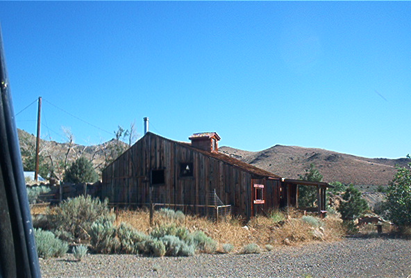 old wooden building with a porch in a desert landscape under a clear blue sky