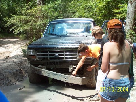 1987 Ford Bronco - A group of people inspect the front bumper of a muddy Ford Bronco.