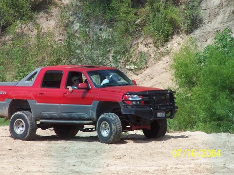 1987 Ford Bronco - A red Chevrolet Avalanche is shown off-road, aftermarket tires and a protective bull bar on the front bumper.