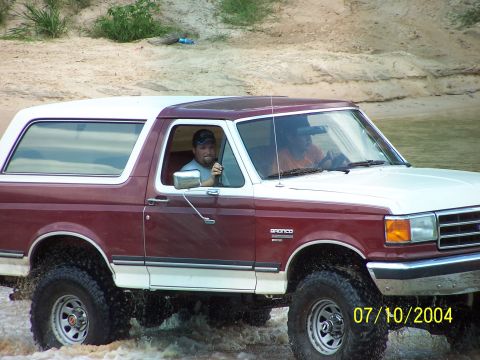 1987 Ford Bronco - A 1987 Ford Bronco navigates through shallow water, with two occupants inside.