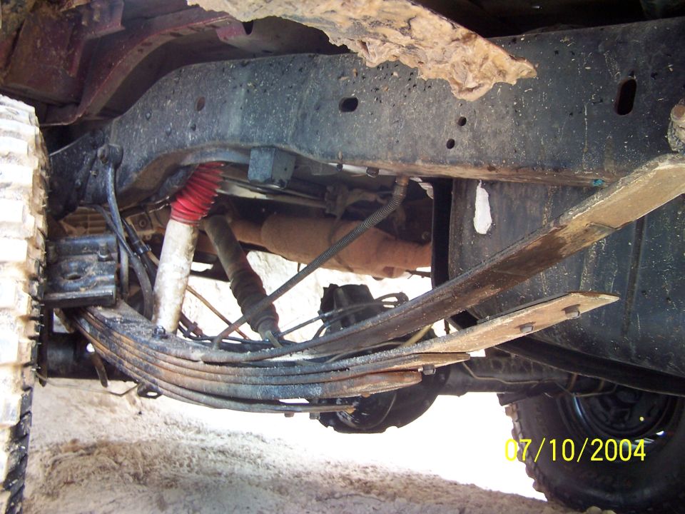 Undercarriage view of a vehicle's suspension and frame, showing leaf springs and a shock absorber