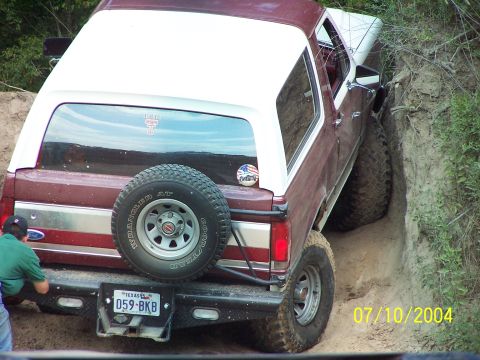 1987 Ford Bronco - A maroon and white 1987 Ford Bronco is stuck in a ditch, with a person attempting to help.