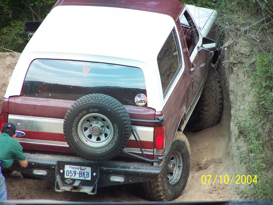 Maroon and white 1987 Ford Bronco with spare tire on rear, stuck in a ditch