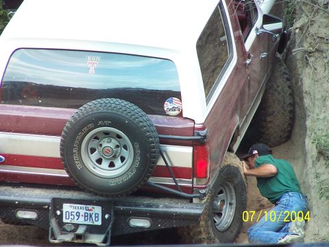 1987 Ford Bronco - A maroon and white 1987 Ford Bronco is seen off-roading, with a person checking the tire.