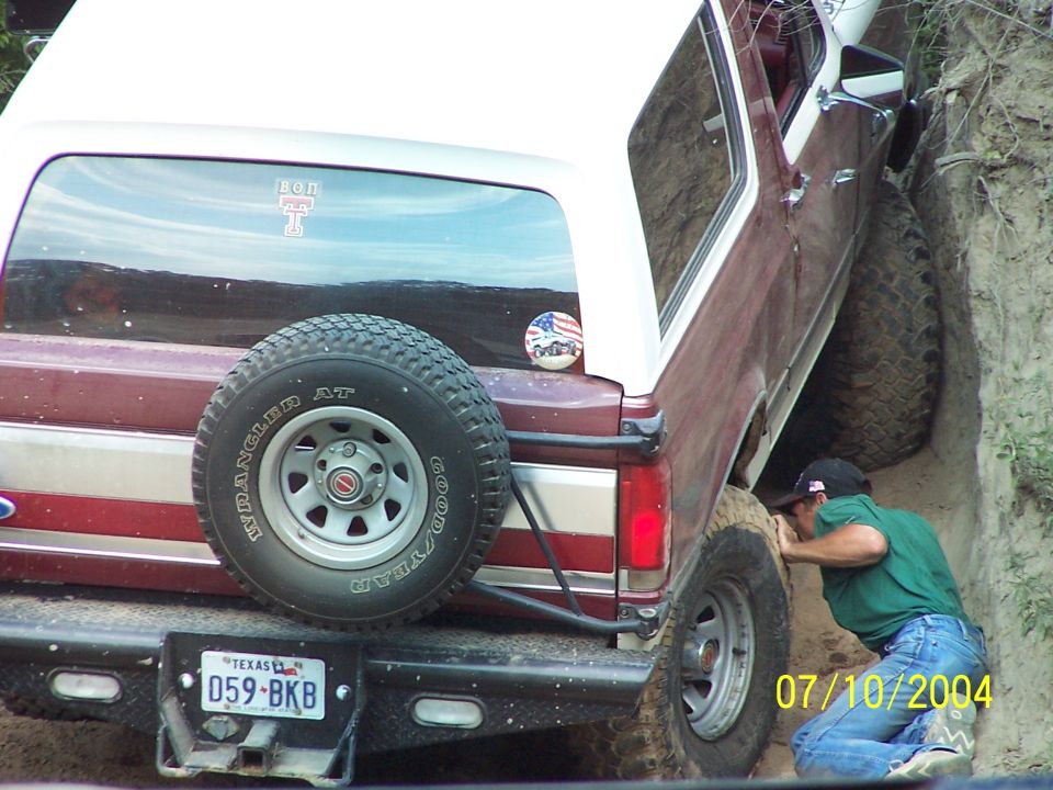 Maroon and white 1987 Ford Bronco off-roading, rear view