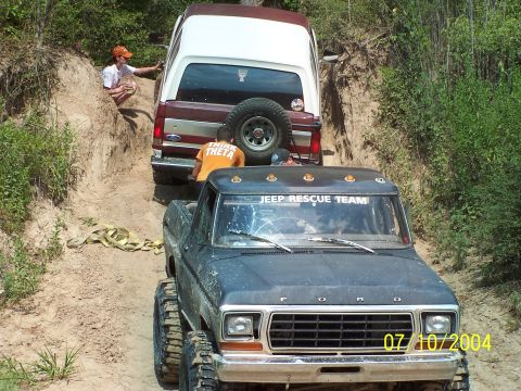 1987 Ford Bronco - Two Ford vehicles navigate a steep, sandy off-road path with vegetation on the sides.