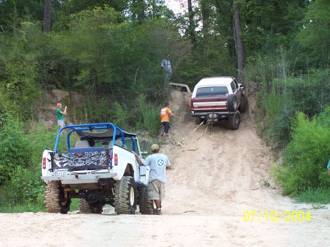 1987 Ford Bronco - Off-road vehicles navigate a challenging dirt incline with onlookers present.