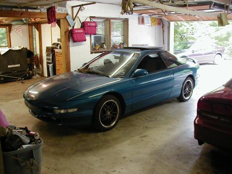 1994 Ford Probe - A teal coupe sits in a garage, partially obscured by a red car and other items.