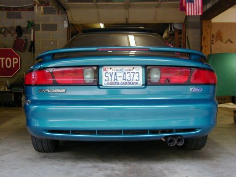 1994 Ford Probe - The rear of a teal Ford Probe is parked in a garage, showing its taillights, spoiler, and dual exhaust.