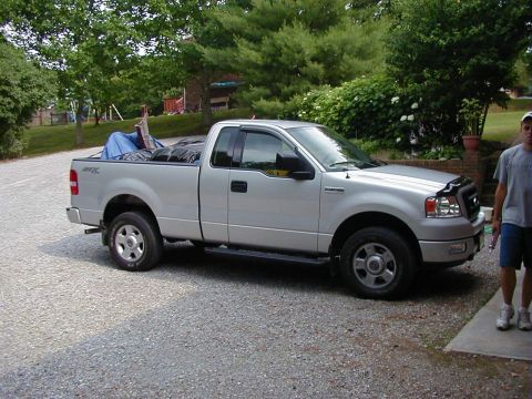 1994 Ford Probe - A silver pickup truck is parked on a gravel driveway with its bed loaded with items covered by a blue tarp.