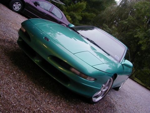 1994 Ford Probe - A green coupe with pop-up headlights is parked on a gravel surface, with another car in the background.