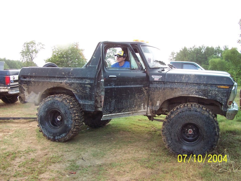 Black Ford Bronco with large tires, driver visible, door open, mud-splattered