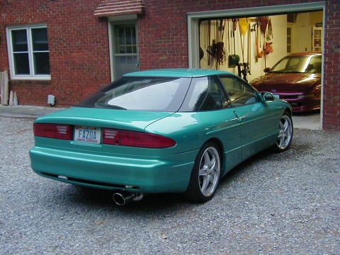 1994 Ford Probe - A teal coupe is parked outside a brick house with a garage containing another vehicle.