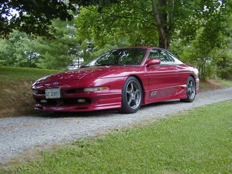 1994 Ford Probe - A red 1994 Ford Probe GT is parked on a gravel driveway, surrounded by lush green grass and trees.