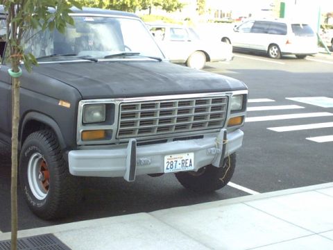 1995 Ford Bronco - Front view of a dark-colored 1980s Ford Bronco parked near a crosswalk.