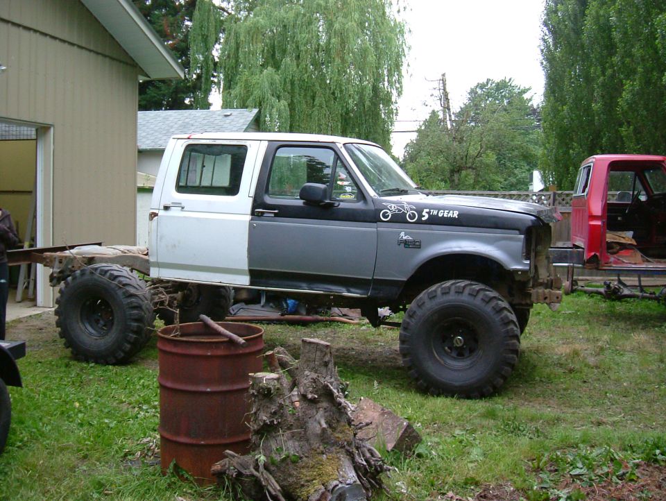 1995 Ford F-150 extended cab chassis, two-tone paint, large tires. Red truck cab visible to the right