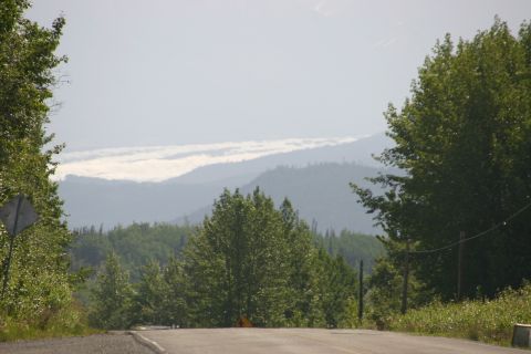 2003 Jeep TJ - A view of a road winding through a landscape with lush green trees and layered mountains in the distance.