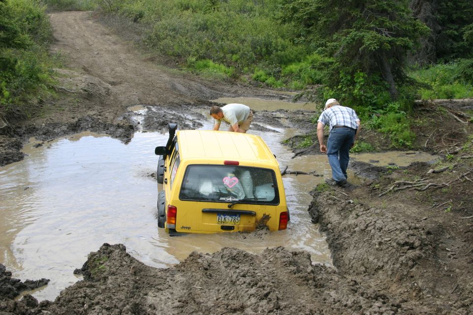 Yellow 2003 Jeep TJ stuck in deep mud with two people nearby