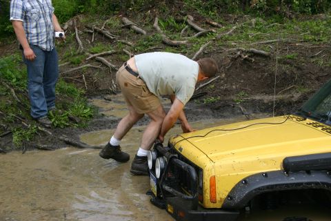 2003 Jeep TJ - A yellow Jeep is stuck in the mud, with a person attempting to push it free.